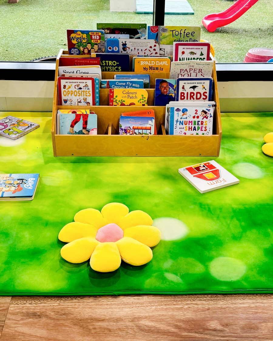 The Blooming Buds book corner, with a low book display and flower cushions on a green rug