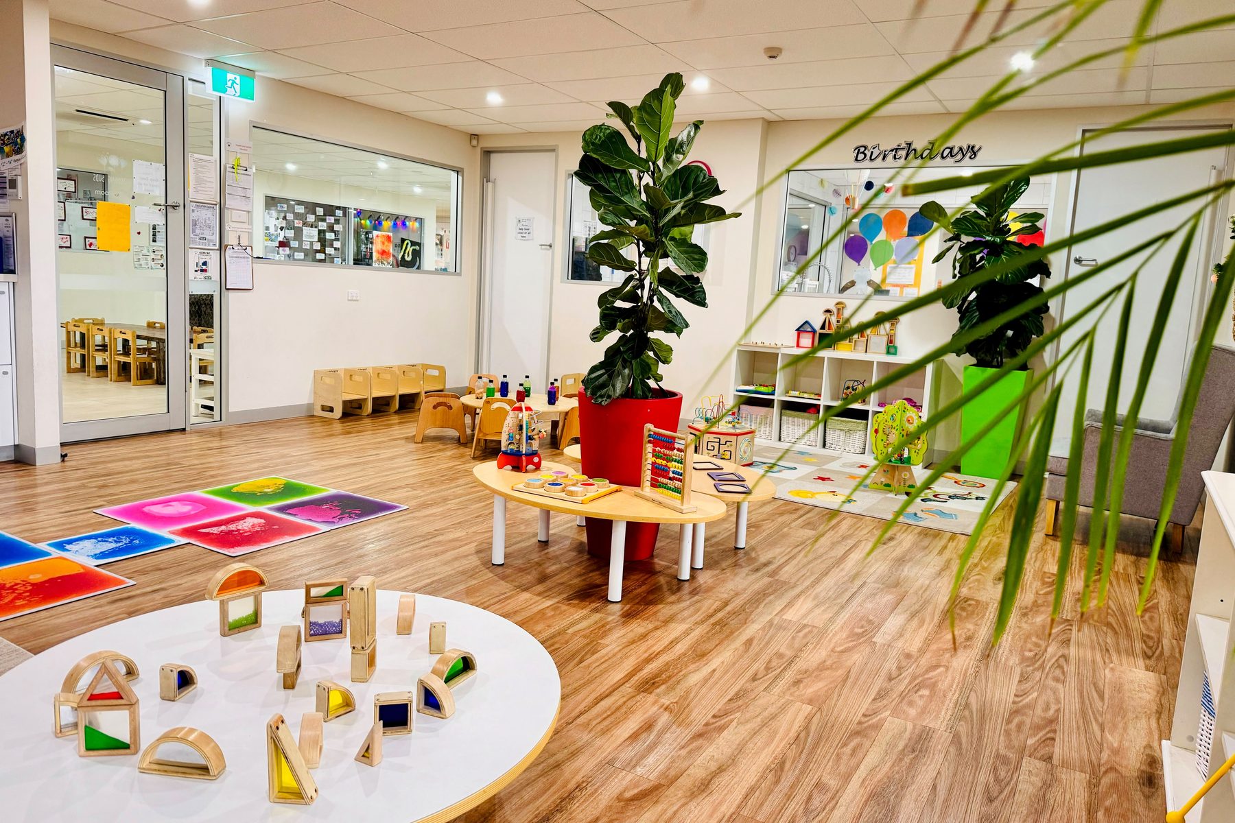 A bright Blooming Buds play room with a light table, wooden blocks, sensory floor tiles and a large indoor plant